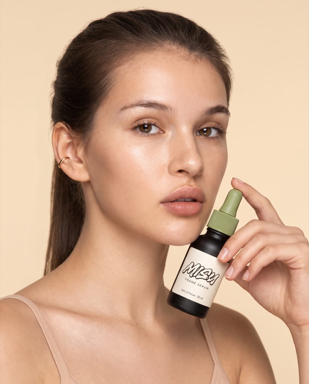 Lora 2 holding the Frame Serum beside her jaw in a cream campaign frame