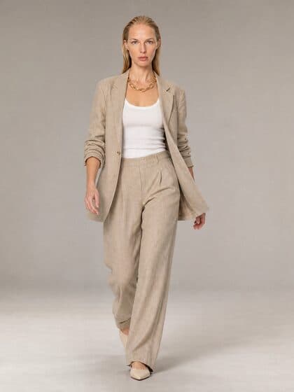 Model in the sand linen blazer walking on a grey studio backdrop, full length