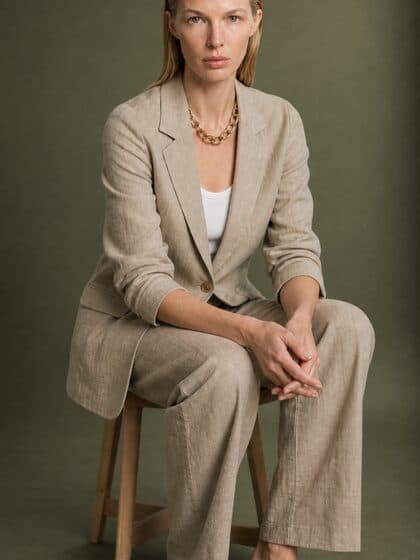 Model in the sand linen blazer seated against a green studio wall