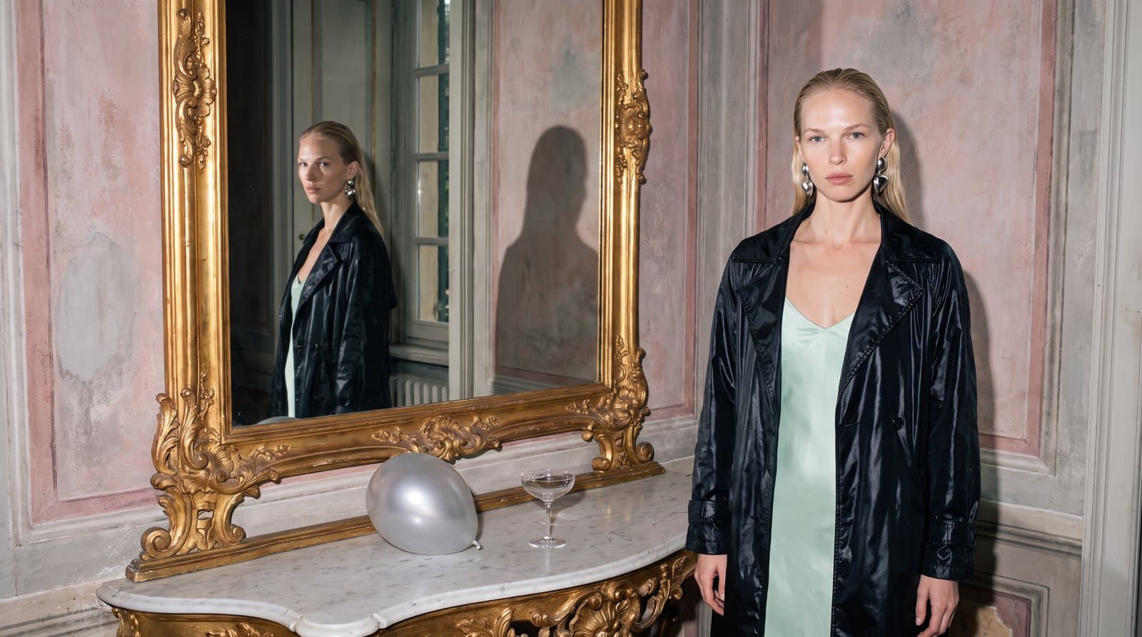 Still of a blonde model at a gilded mirror whose reflection looks into the lens