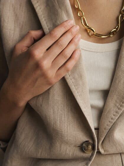 Close detail of the sand linen blazer button, hand and necklace