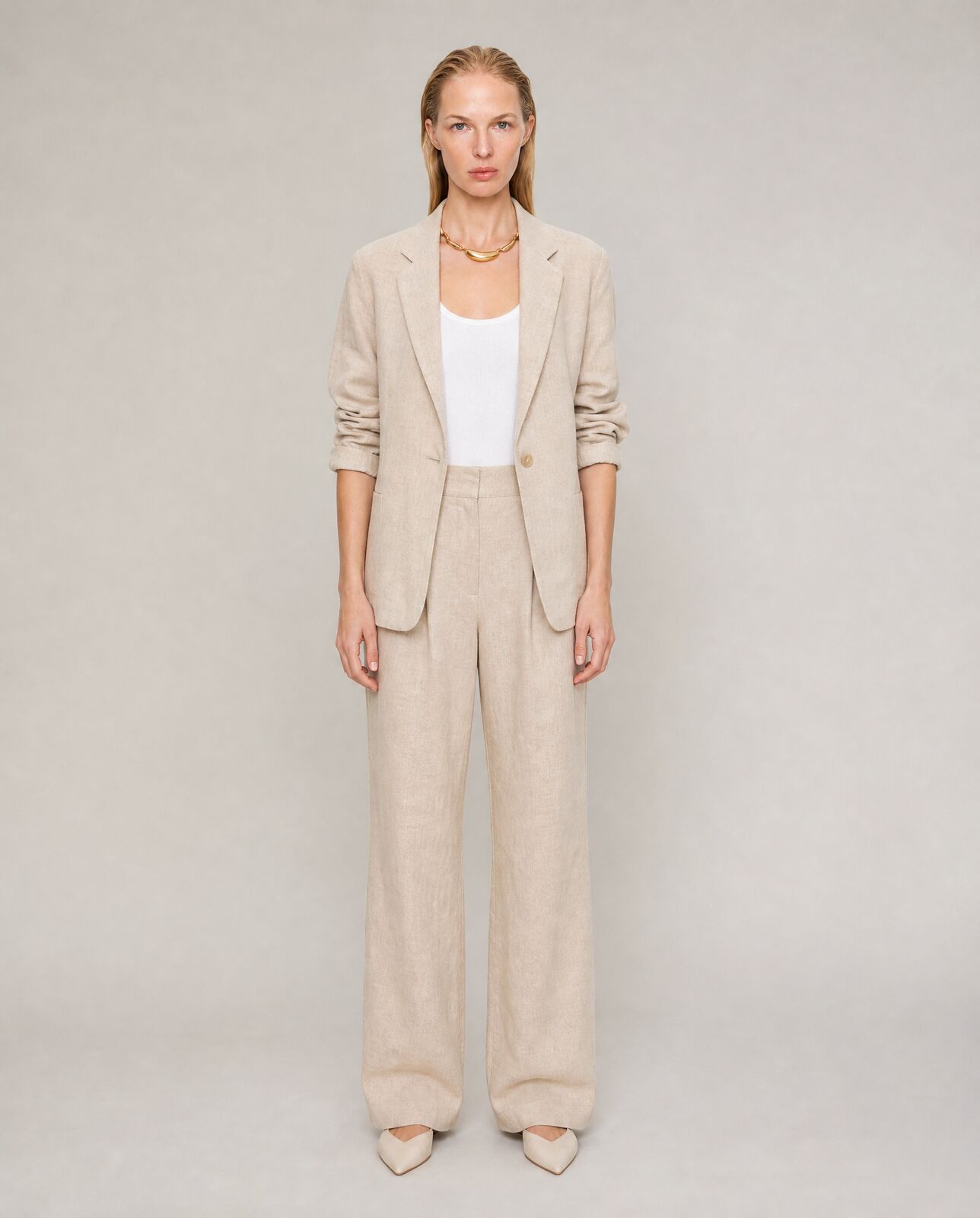 Full-length e-commerce image of a model in a beige linen suit and white tank, standing straight on against a light grey background.